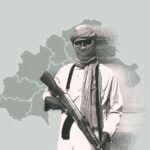A masked armed militant in traditional Sahelian clothing holds a rifle in front of a map outline of Burkina Faso, symbolizing jihadist presence in the region.