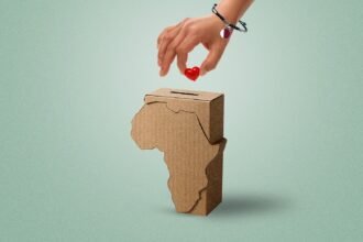 A stylized image of a hand wearing a Qatar-flag bracelet placing a red heart into a donation box shaped like the African continent. The background is clean and minimalistic, symbolizing clarity and focus on giving.