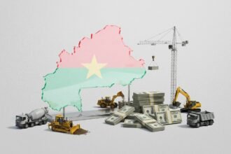 Unfinished flyover on the outskirts of Ouagadougou with concrete pillars above busy traffic, symbolising Burkina Faso’s $64‑billion bet on new infrastructure and economic transformation amid insecurity
